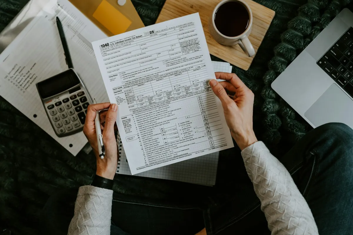 Manos sosteniendo formularios de la declaracion de la renta junto a una calculadora